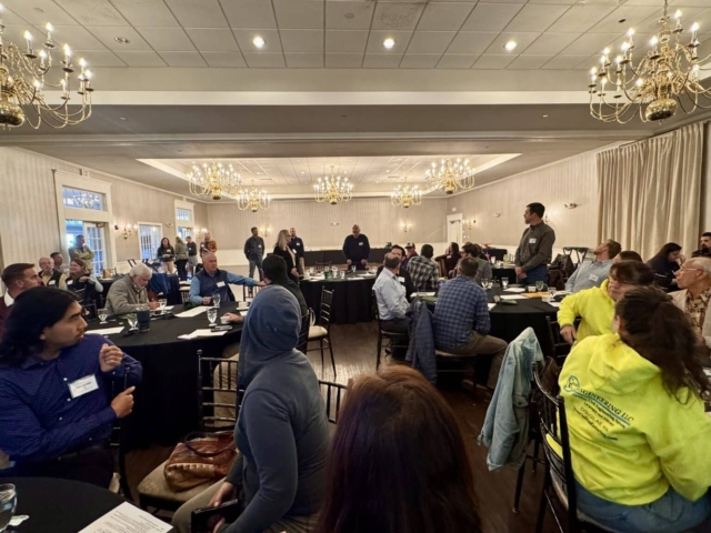 Attendees seated at round tables listening to a speaker at the AMWS annual meeting.